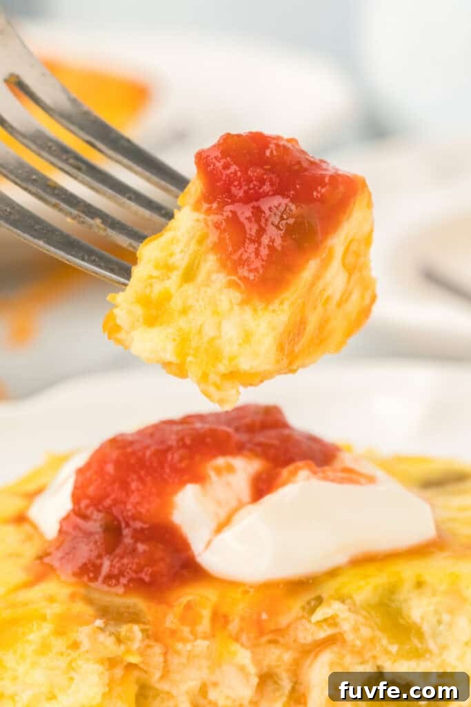 Fork holding a bite of Chilies Rellenos Bake topped with salsa above the casserole