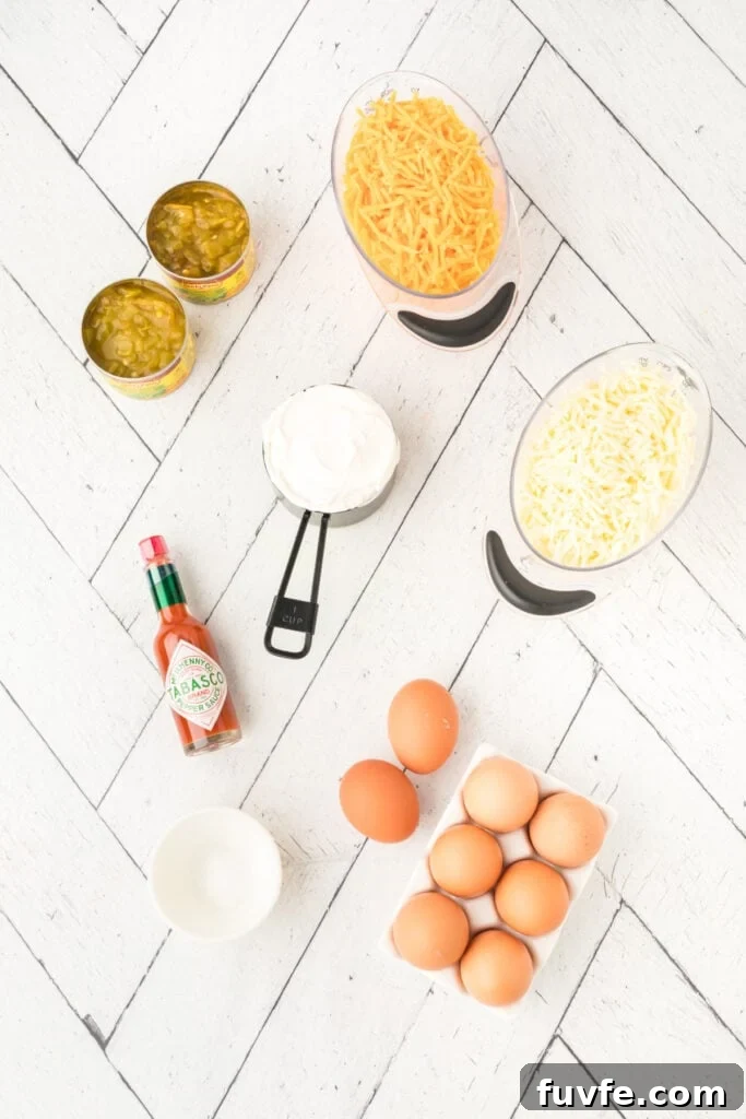 Ingredients for Chilies Rellenos Bake including eggs, shredded cheese, sour cream, green chilies, and hot sauce on a white surface