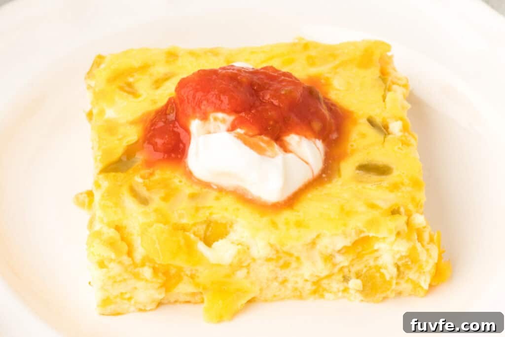 Slice of Chilies Rellenos Bake topped with sour cream and salsa on a white plate