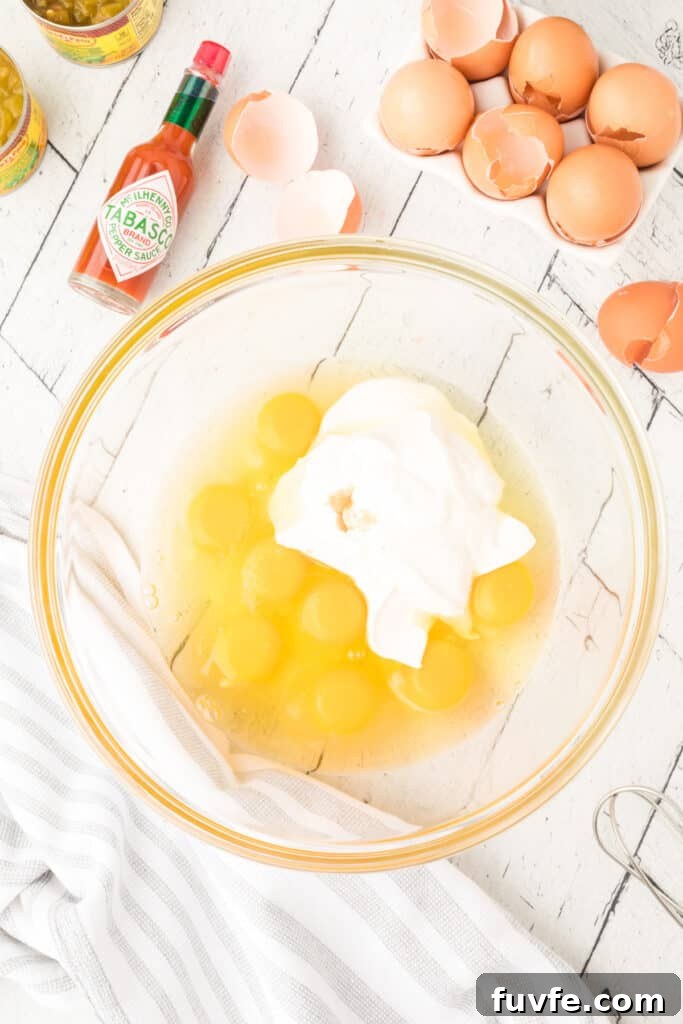 Eggs, sour cream, salt, and hot sauce in a glass mixing bowl for Chilies Rellenos Bake
