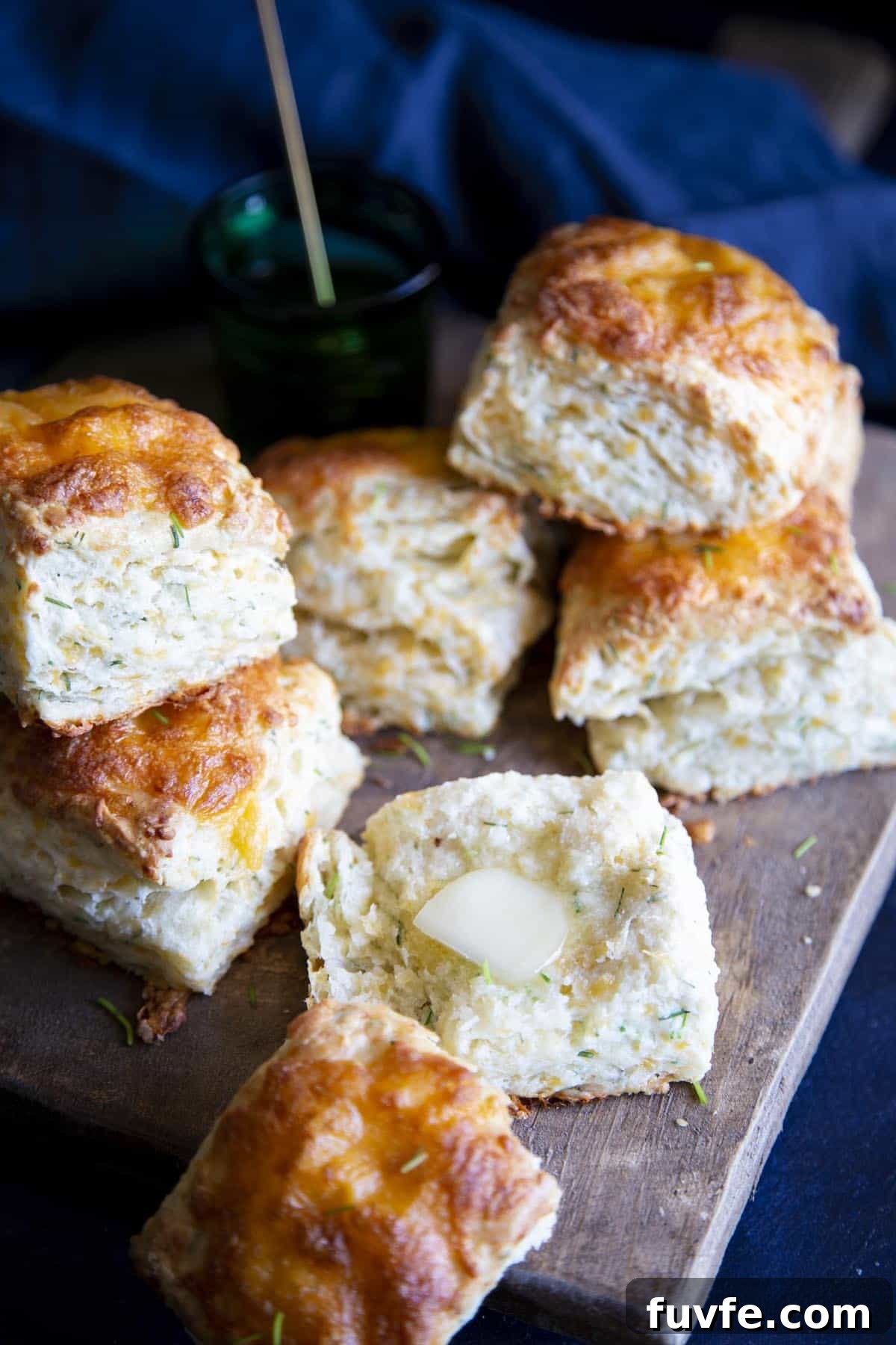 Cheese biscuits on a wooden board, one is broken open with a pat of butter on it.