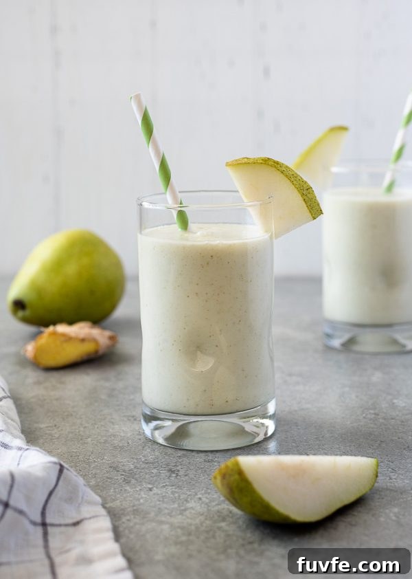 Silky Pear and Ginger Smoothie Recipe 2 pear smoothie with slice of pear on the top of the glass and green striped straw