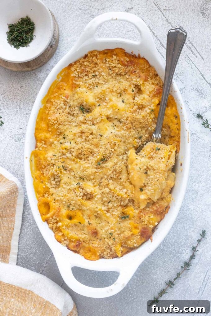Baked butternut squash mac and cheese in baking dish with a spoon.