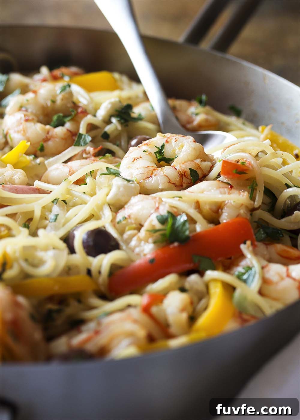Close-up of a spoon serving a portion of shrimp and pasta from a large saute pan.