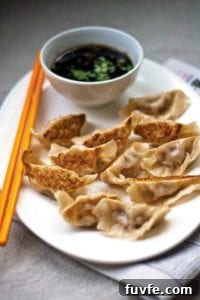 A white oval plate filled with pot stickers, a pair of chopsticks, and dipping sauce.