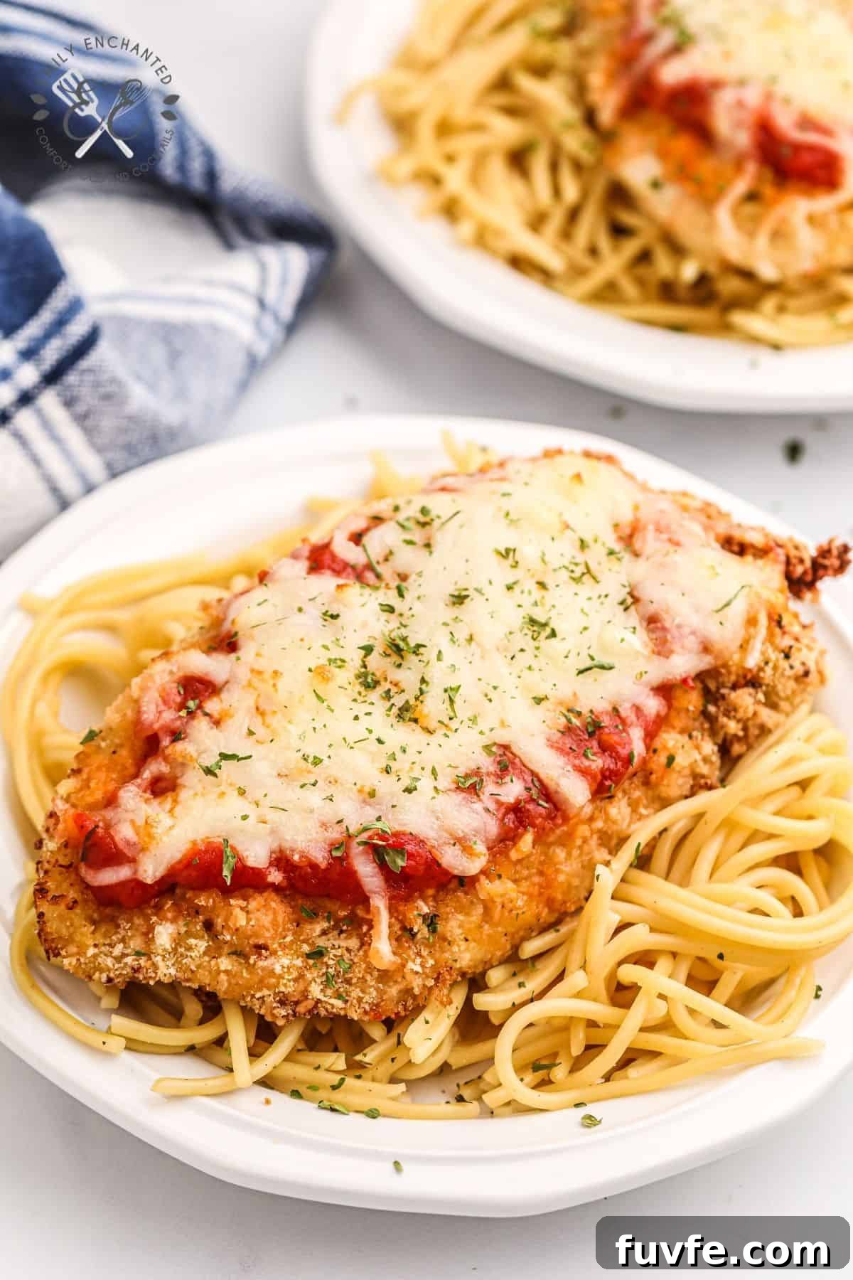 Air Fryer Chicken Parmesan on spaghetti on a white plate with blue checkered towel in background