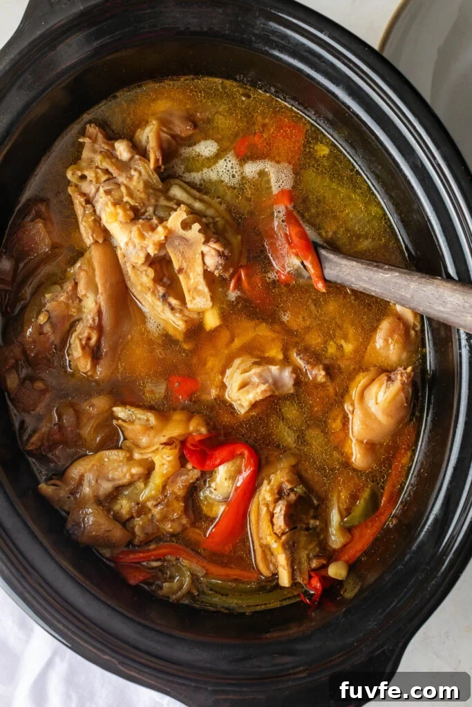 Crockpot with Pigs Feet, red peppers, and a wooden spoon.