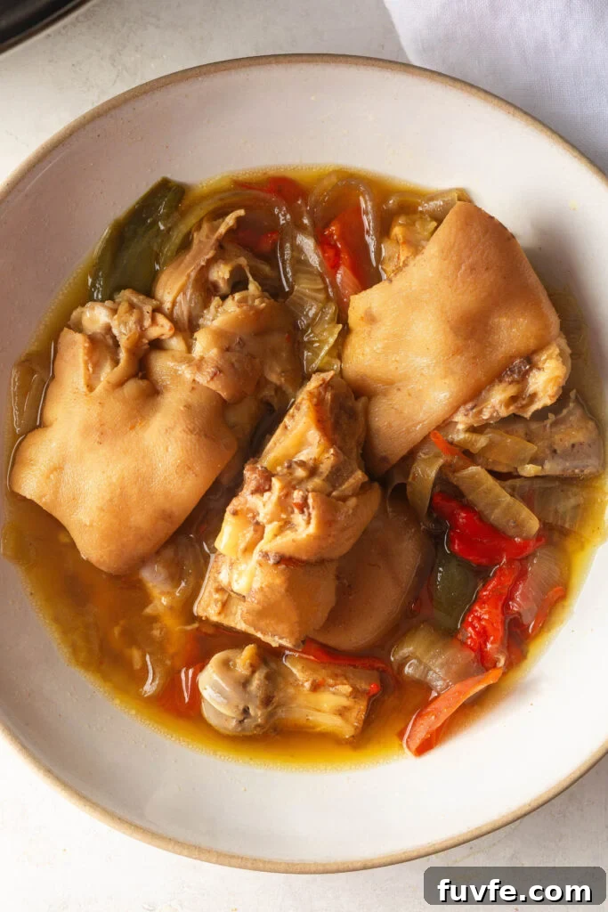 White bowl with Pigs Feet, onions, red bell pepper, green bell pepper, and braising liquid.