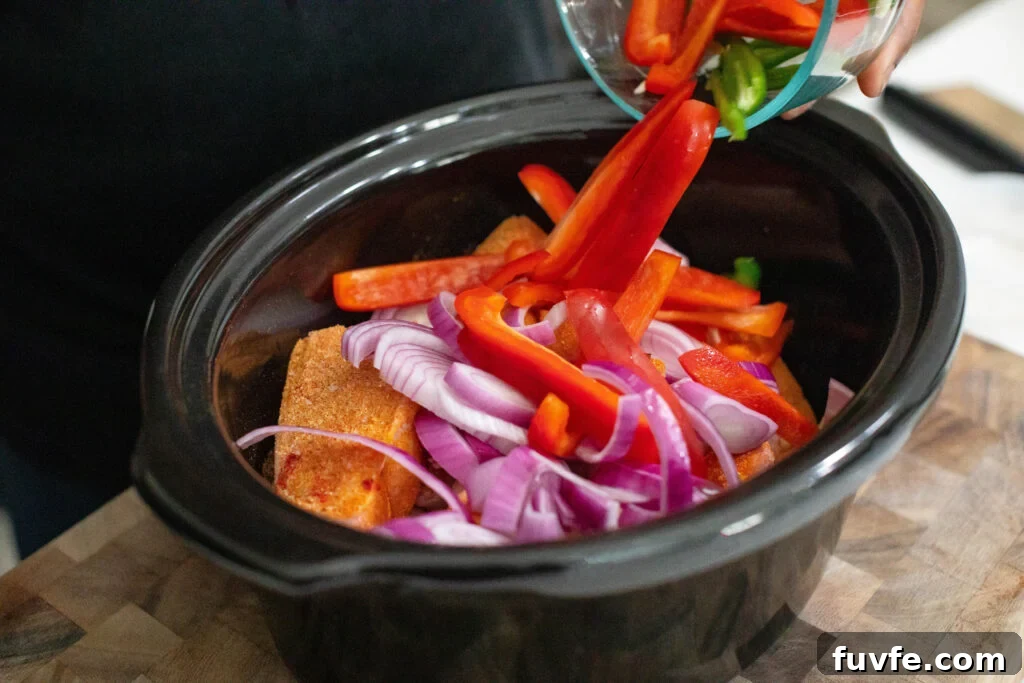 Adding in sliced red onion, red bell pepper, Jalapeño, and garlic to crock pot with seasoned Pigs Feet.
