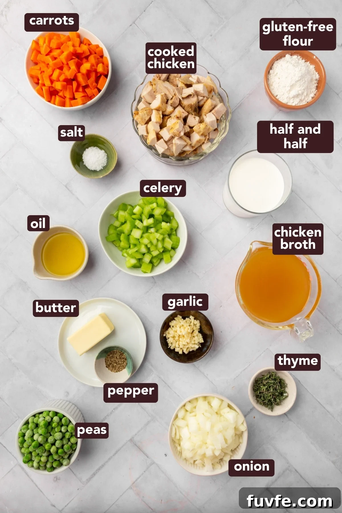 Top-down view of various labeled ingredients in bowls on a white surface, including carrots, cooked chicken, gluten-free flour, half and half, chicken broth, celery, salt, oil, butter, garlic, thyme, onion, pepper, and peas.