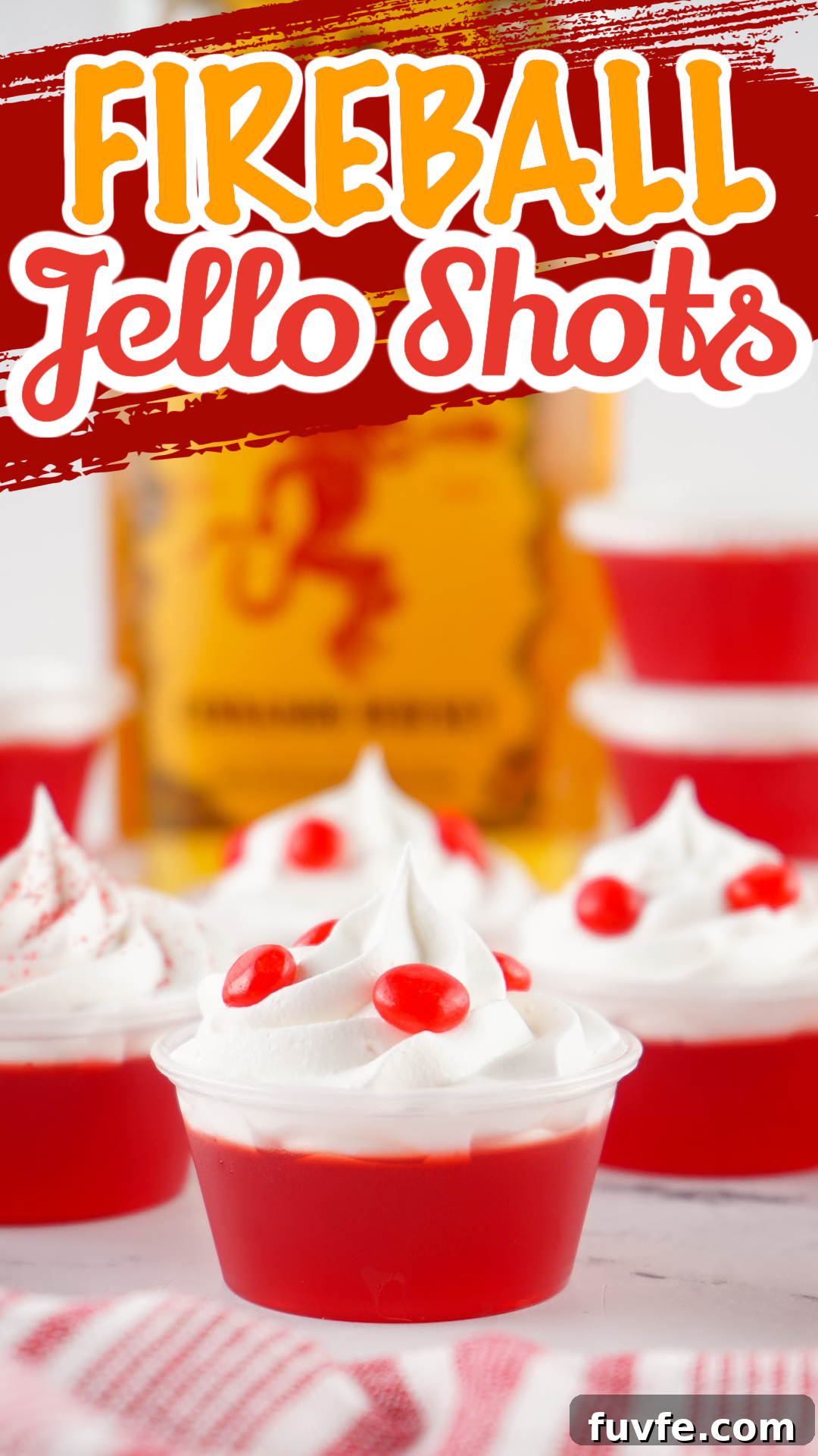 Red fireball jello shots with a bottle of Fireball in the background. Topped with whipped cream and red hot candy.