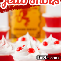 Red fireball jello shots with a bottle of Fireball in the background. Topped with whipped cream and red hot candy.
