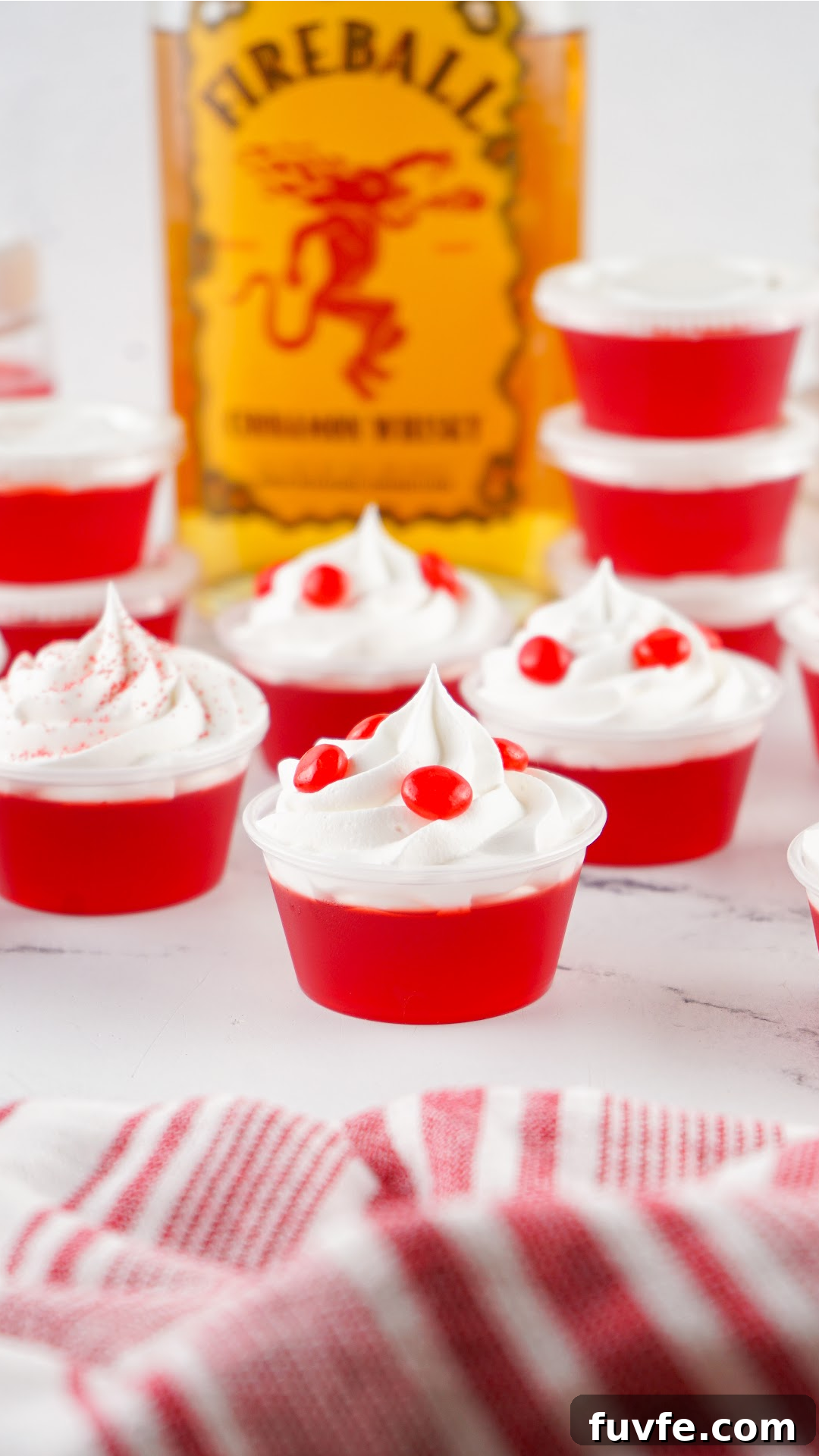 Red fireball jello shots with a bottle of Fireball in the background. Topped with whipped cream and red hot candy.