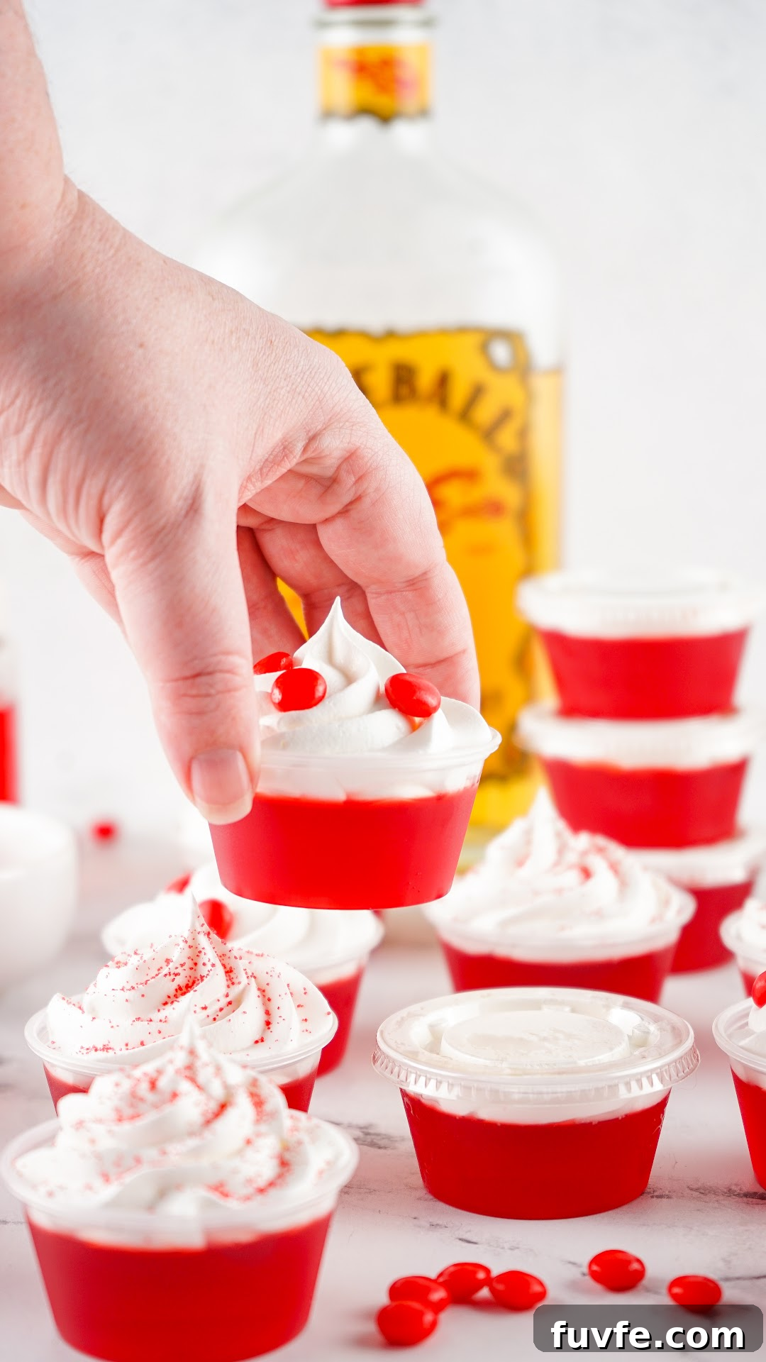 Cherry fireball jello shots with a bottle of Fireball in the background. Topped with whipped cream and red hot candy.