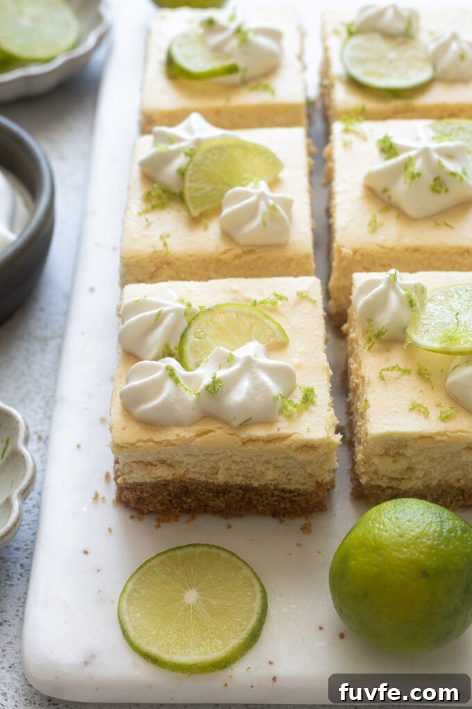 Key lime cheesecake bars with piped whipped cream and lime slices.