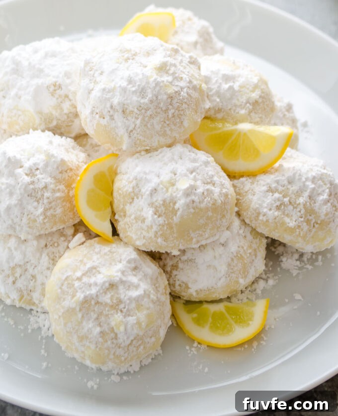 Meyer Lemon Kourabiedes Recipe: Greek Butter Cookies 7 Kourabiedes piled on a plate with slices of lemon.